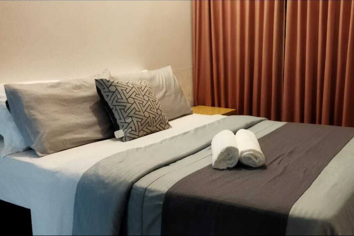 Un lit bien fait, avec un oreiller à motifs, une serviette pliée et une table de chevet en bois à côté.