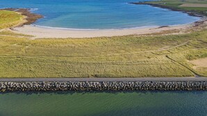 An aerial view of a coastal area with a road leading to a beach, surrounded by grassy fields and a body of water. - Studio House (Saint Margaret's Hope)