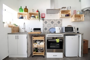 A compact kitchen with built-in appliances, wooden shelves with dishes, and a tiled backsplash.