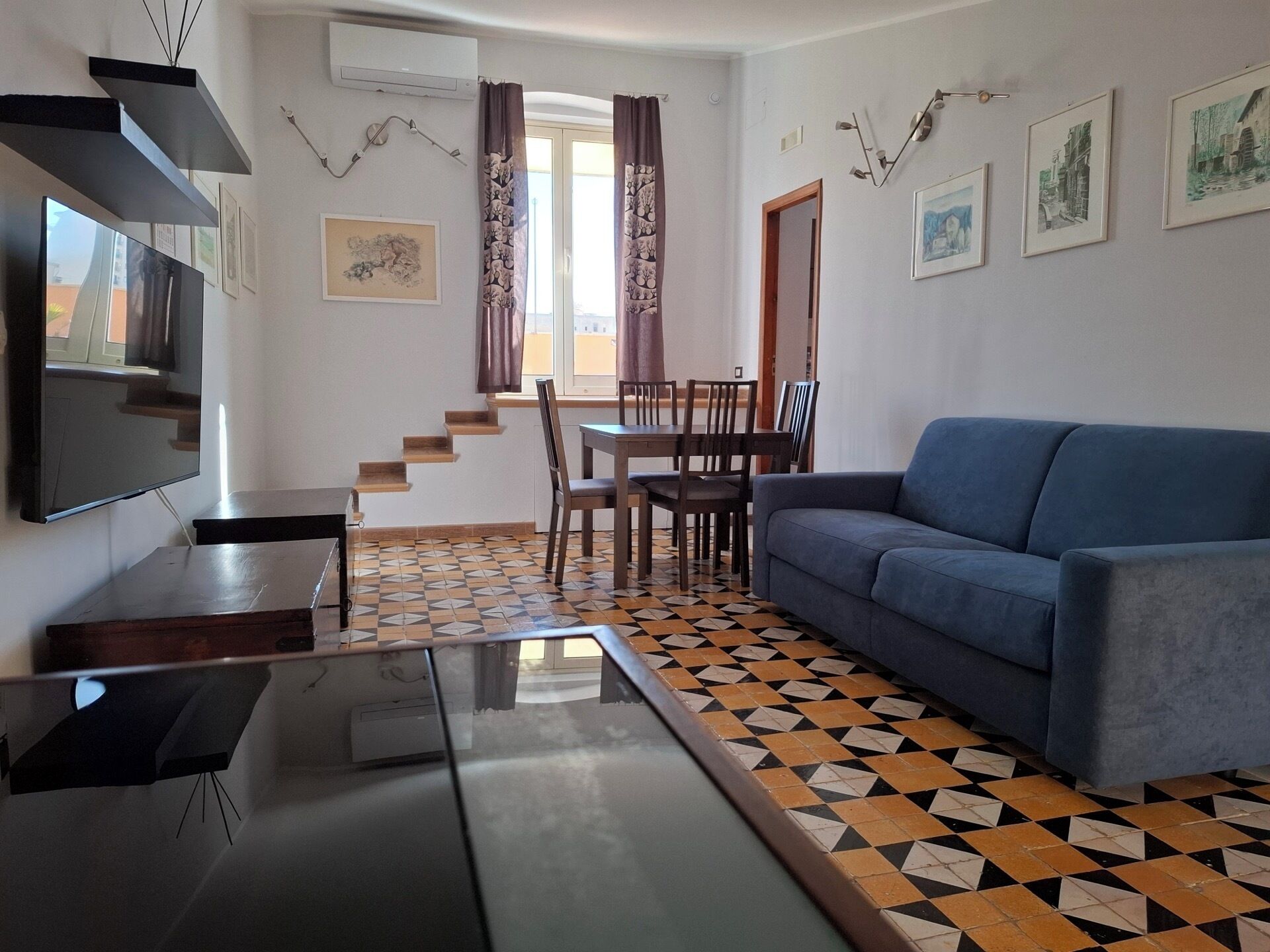 A living room with a TV, a sofa, a dining table with chairs, and a staircase.
