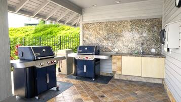 An outdoor kitchen area with two barbecue grills, a granite countertop, and a sink.