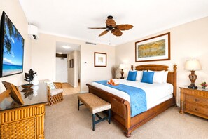 Une chambre à coucher avec un lit, un ventilateur de plafond, une table de chevet, une lampe, un cadre photo et une vue sur la plage.