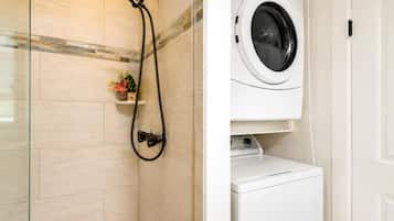 A bathroom with a shower, a washing machine, and a small shelf with flowers.