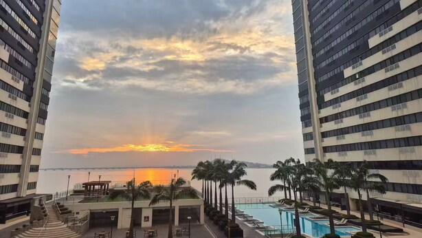 A high-rise hotel with a pool area, palm trees, and a sunset view.