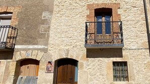 A rustic building with a stone facade, a wooden door, and a balcony with wrought iron railings.