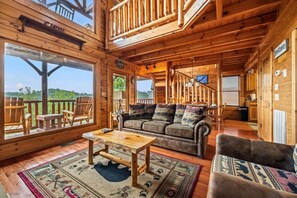 A wooden cabin interior with a sofa, chairs, a table, and a view of the outdoors.