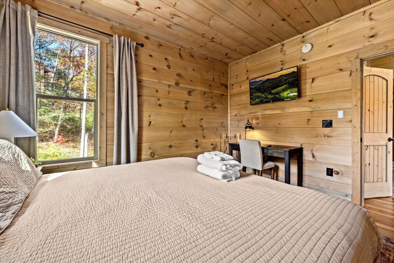 Camera da letto in una baita di legno, con un letto grande, una scrivania e un televisore appeso al muro.