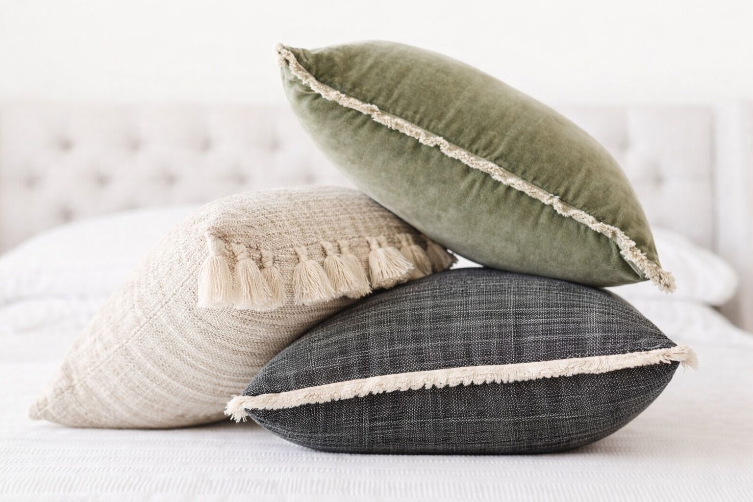 Three pillows with tassels on a bed.