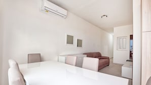 Un salon moderne et minimaliste, avec une table à manger blanche, un canapé et un petit coin cuisine.