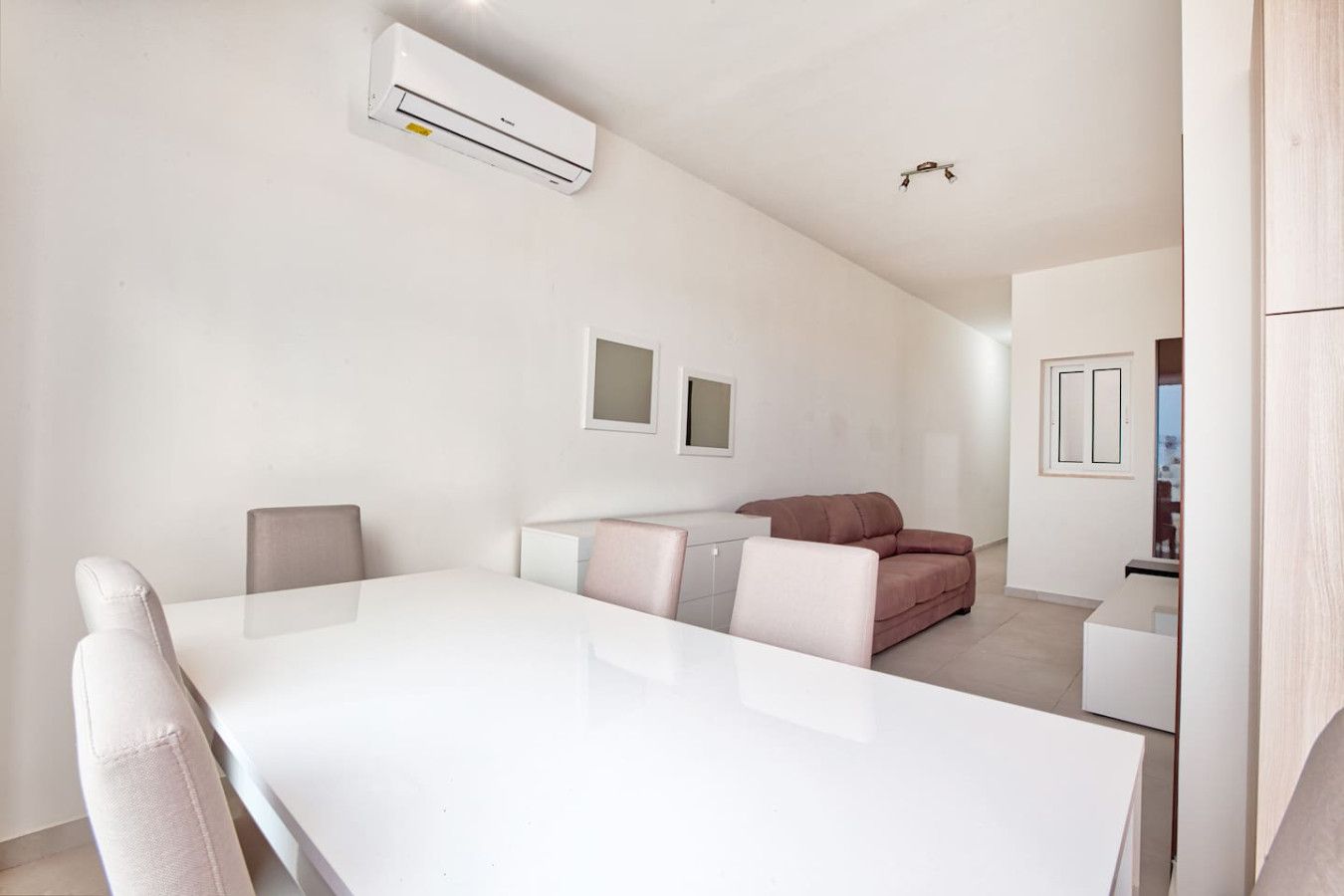 A modern, minimalist living room with a white dining table, a sofa, and a small kitchen area.