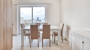 Un espace de restauration moderne avec une table et des chaises blanches, de grandes fenêtres offrant une vue sur la ville et un design minimaliste.