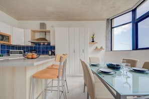 A modern kitchen with white cabinets, blue tiles, and a glass dining table with chairs. - Corner Stay / Sea Front / Terrace / Parking (Tas-Sliema)