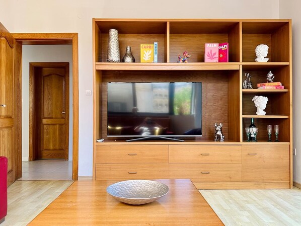 Een woonkamer met een grote flatscreen-tv, houten planken met decoratieve items en een houten kast met lades.