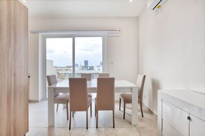 Un comedor moderno con una mesa y sillas blancas, ventanas amplias con vistas a la ciudad y un diseño minimalista.