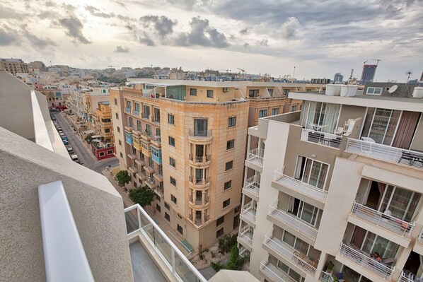 A multi-story residential building with balconies, a street view, and a cloudy sky.