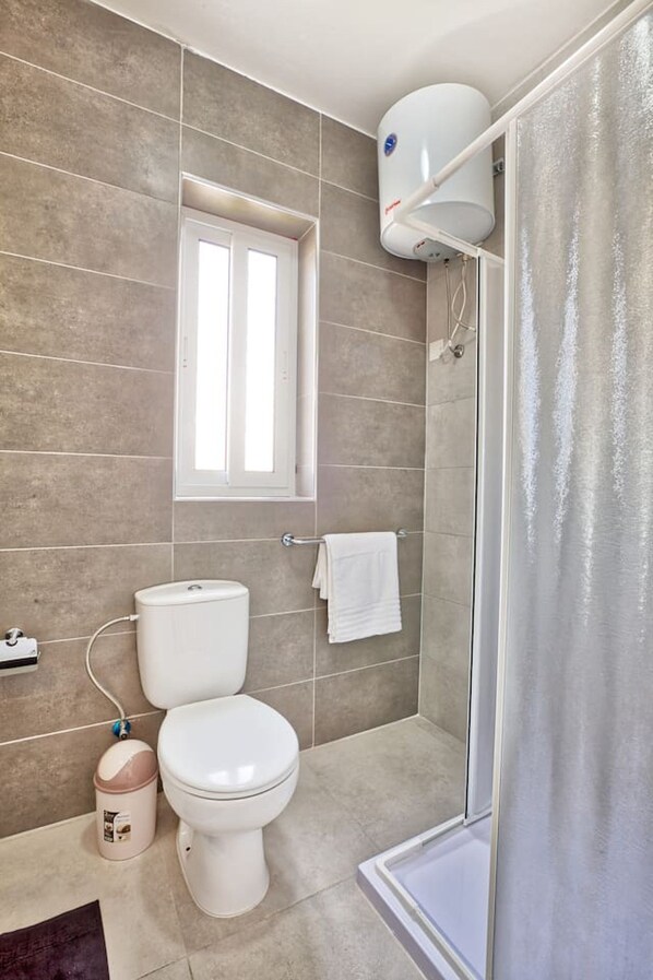 Un baño con inodoro, ducha y ventana.