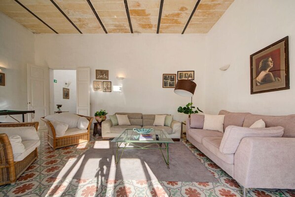 Ein Wohnzimmer mit einer Couch, einem Couchtisch und einer Lampe. An den Wänden hängen Bilder in Rahmen und im Hintergrund ist eine Tür zu sehen.