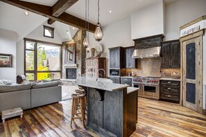 A spacious kitchen with a large island, dark wooden cabinets, and a stone fireplace.