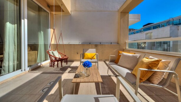 A balcony with a sofa, chairs, a hanging chair, and a table with a vase.