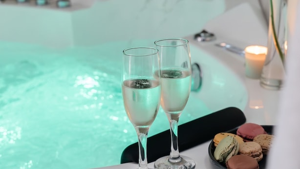 Wellnessbereich mit Whirlpool, zwei Sektgläsern, einer Rose und Macarons auf einer Platte.