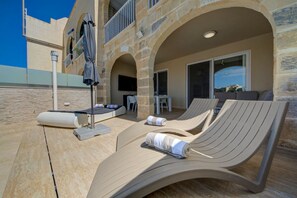 A sunlit outdoor lounge area with two reclining chairs, a small table, and a covered seating area.
