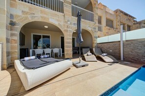 A poolside area with a bed, lounge chairs, and a dining area. - Oakville +, Private Pool & BBQ & Games Room (Xagħra)