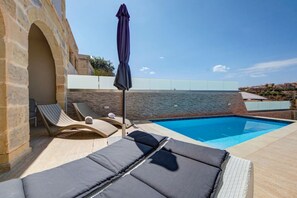 A poolside area with lounge chairs and a stone wall. - Oakville +, Private Pool & BBQ & Games Room (Xagħra)