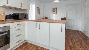 A modern kitchen with white cabinets, a wooden countertop, and a microwave. There are two framed pictures on the wall and a door to the right. - Pass the Keys | Modern | Office & Driveway | Near Crook & Durham (Crook)