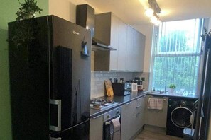 Une cuisine compacte équipée d’un réfrigérateur, d’une cuisinière, d’un évier et d’une fenêtre donnant sur un espace verdoyant.