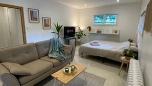 A modern living room with a sofa, a coffee table, a TV, and a bed. - Havre de paix à Itteville - nature & comfort (Itteville)