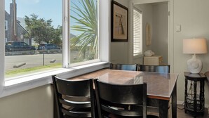 A dining area with a table and chairs, a window with a view of the street, and a lamp on a side table. - The Tides by the Sea - Entire rental unit in Seaside, Oregon, United States (Seaside)