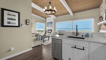 A kitchen with a view of the ocean, wooden ceiling beams, and a chandelier.