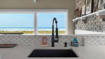 A kitchen with a view of the ocean, a black faucet, and a soap dispenser.