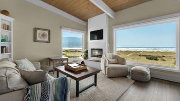 A spacious living room with a fireplace, large windows overlooking the beach, and a cozy seating area.