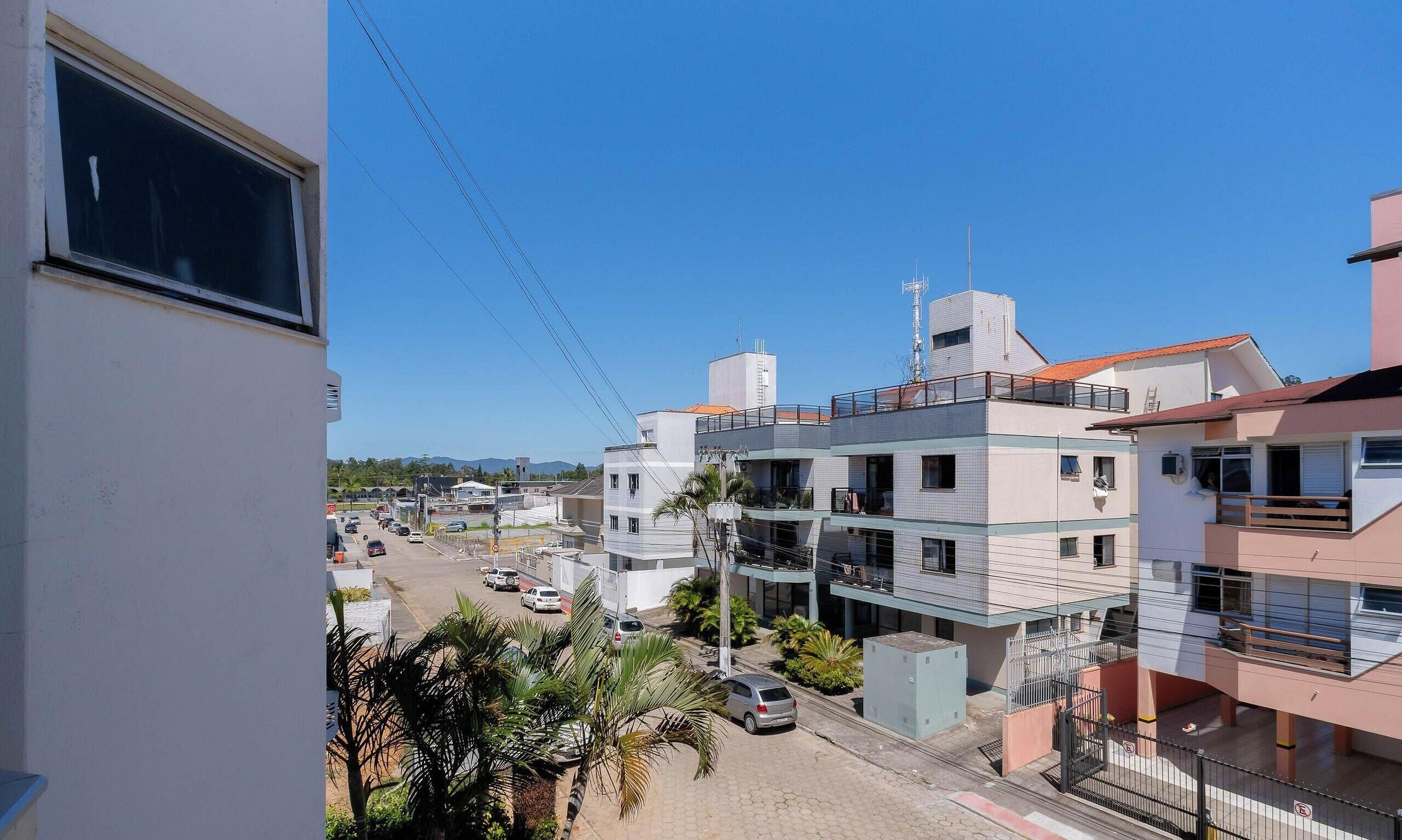 A residential area with multi-story buildings, a clear sky, and a street with parked cars.