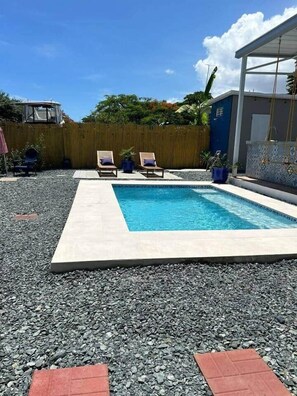 Una piscina rectangular con dos sillas de descanso y un muelle de madera.