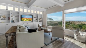 A spacious living room with a large TV, white cabinetry, and a view of the beach.