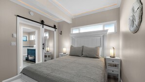 A bedroom with a large bed, bedside tables, a nightstand, a window, and a door leading to a bathroom.