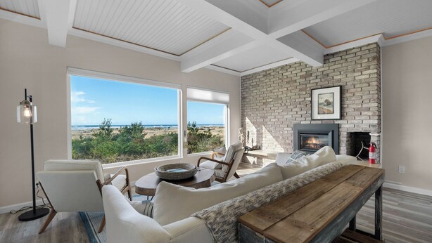 A spacious living room with a large window overlooking a beach, a fireplace, and a cozy seating area.