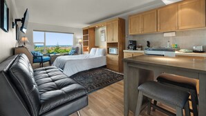 Una habitación de hotel moderna con una cama grande, una zona de estar con sofá de cuero y un taburete de bar, una kitchenette y vista a la playa.