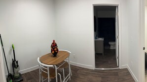 A room with a wooden dining table, chairs, a fruit bowl, a vacuum cleaner, a TV, and a bed. - Delightful apt with AC near historic Midland St district, office, tiled shower (Bay City)