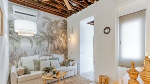 A living room with a white sofa, a coffee table, and a wooden side table. There is a wall mural of palm trees and a ceiling with exposed beams. - Abele 45 by Stay Belonio (Málaga)