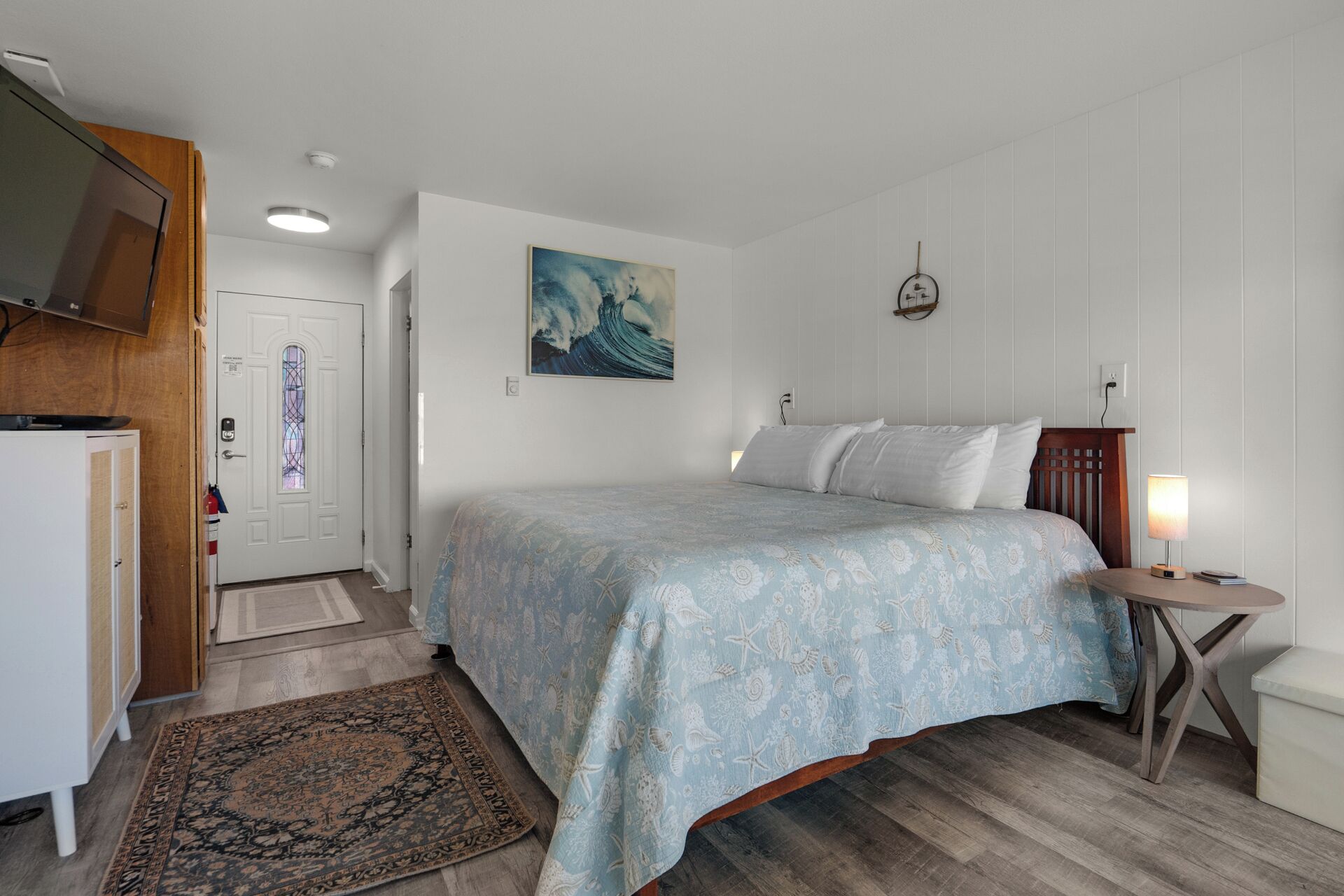 Un dormitorio con una cama, una mesita de noche, una alfombra, un cuadro y una puerta.
