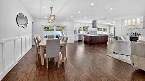Una cocina amplia con armarios blancos, un comedor con una mesa y sillas de madera, y una sala de estar con sofá y alfombra.