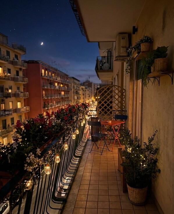 A balcony with outdoor seating, potted plants, and string lights.