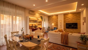 A modern living room with a sofa, dining table, and a TV. - Kyntherland House The ideal location to immerse yourself in a relaxing vacation (Napoli)