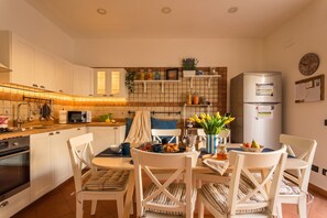 Una cocina con armarios blancos, microondas, refrigerador y comedor con mesa y sillas.