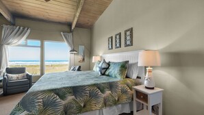 Un dormitorio con una cama grande, dos lámparas de noche, una silla y vistas a la playa.