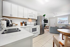 A modern kitchen with white cabinets, stainless steel appliances, and a dining area with a round table and wicker chairs.