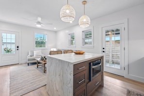 A modern kitchen with a marble island, wooden cabinets, and pendant lights.